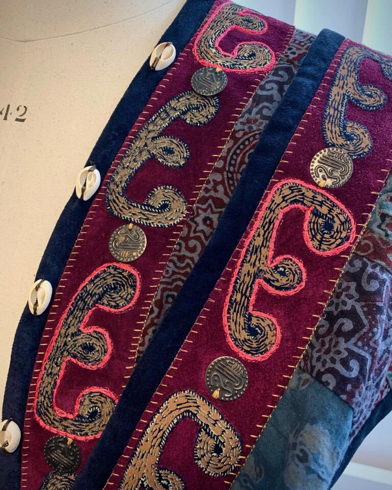 A beaded band of paisley embroidery on indigo and crimson silk, finished with cowrie shells
