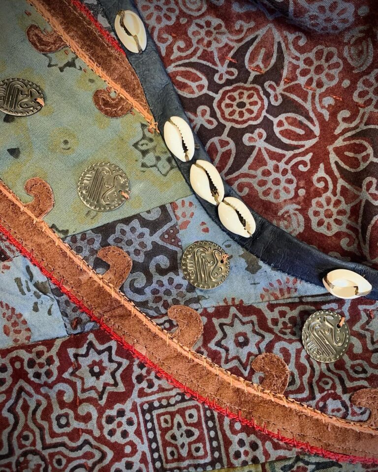 A curved embroidered border in gold and red thread, edged with stitched cowrie shells