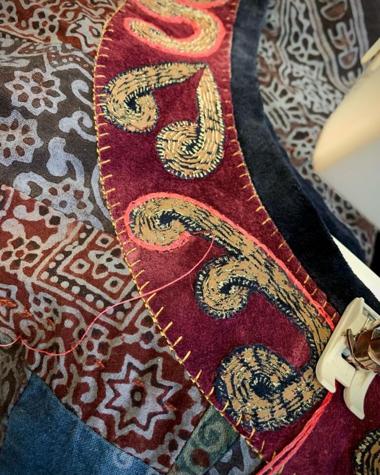 Dense gold paisley embroidery worked onto deep red silk, meeting a patterned block-printed panel