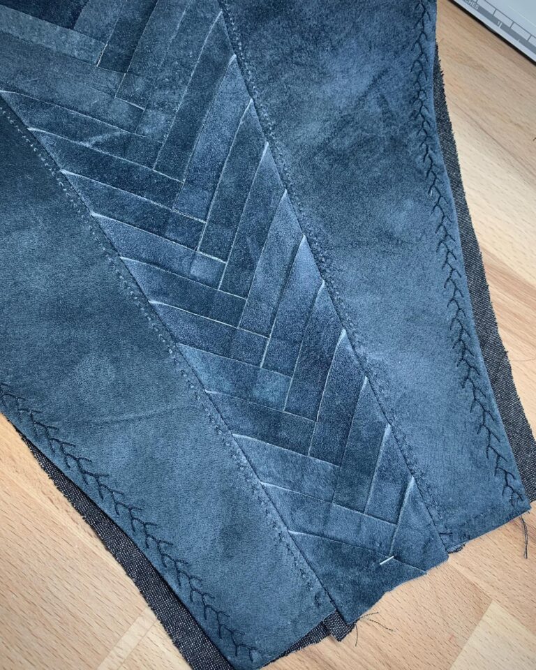 Overlapping suede panels pinned into a diagonal seam, seen from above on the workroom floor